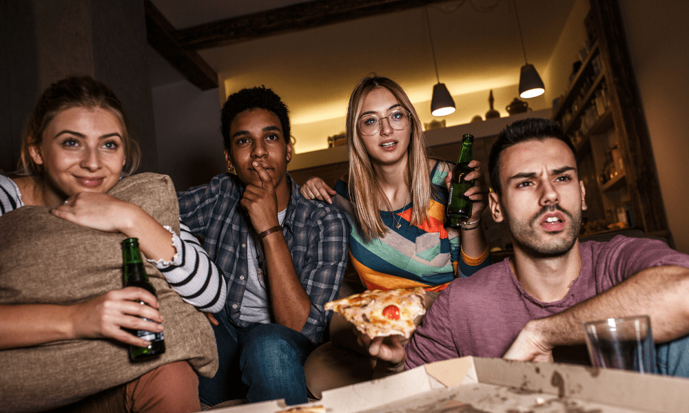 gruppe med fire personer som spiser, drikker og ser på tv